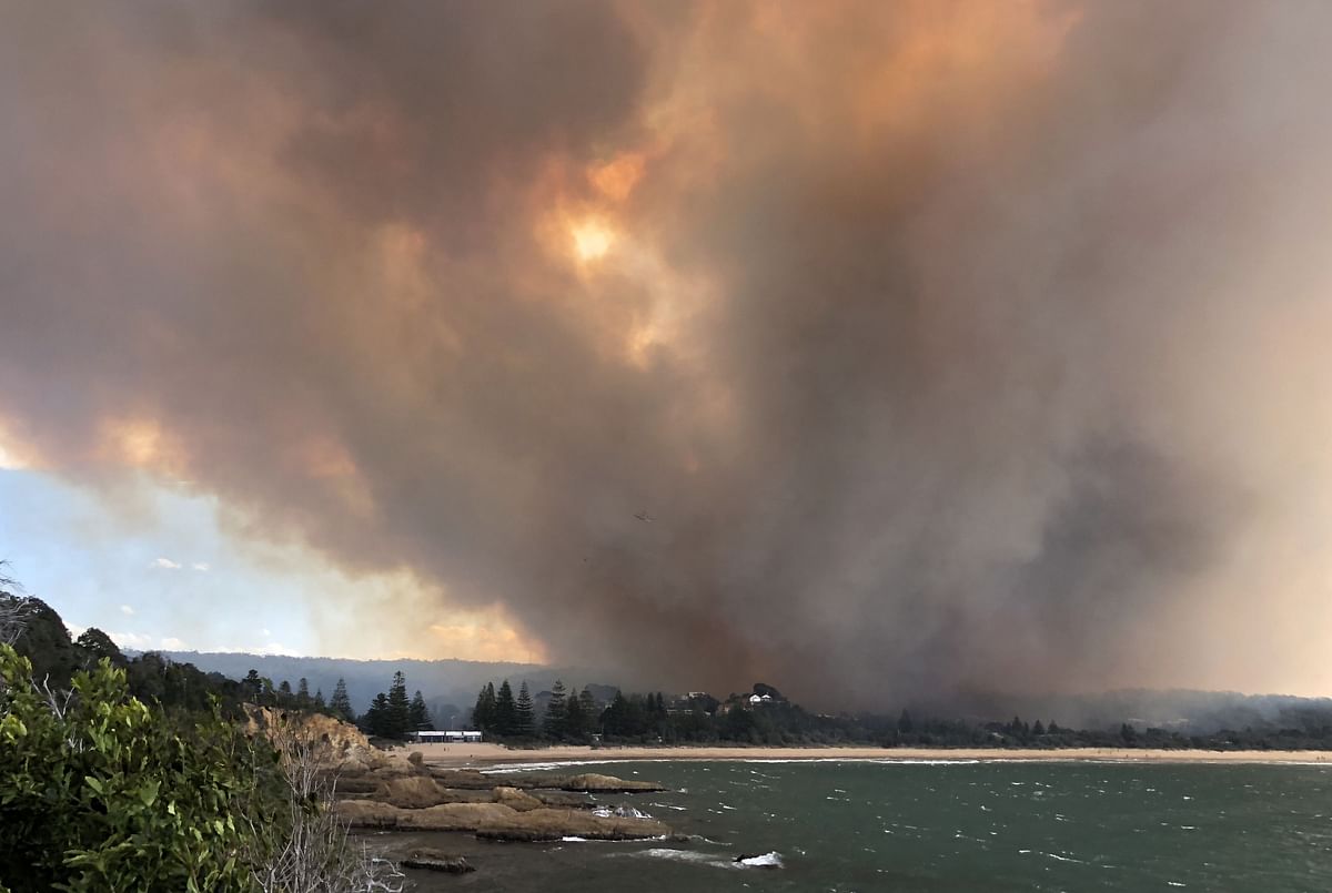 This handout photo taken on 18 March 2018 and received on 19 March shows smoke rising from fires in the village of Tathra on the south coast of New South Wales. Up to 70 homes and buildings were damaged or destroyed in the picturesque seaside village when a fire tore through the area as high temperatures and strong winds have fuelled large grass and bushfires in Australia, officials said on 19 March 2018, reducing dozens of houses to ash and killing cattle.