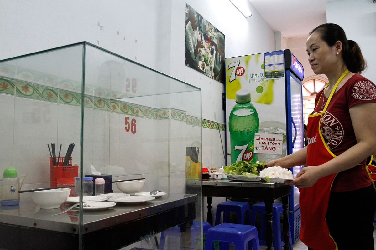 In this photograph taken on 20 March 2018, a waitress carries dishes to customers next to the glass-encased table where former US President Barack Obama sat at for a meal with chef Anthony Bourdain at Bun Cha Huong Lien restaurant, now dubbed `bun cha Obama`, in Hanoi`s old quarter. Photo: AFP