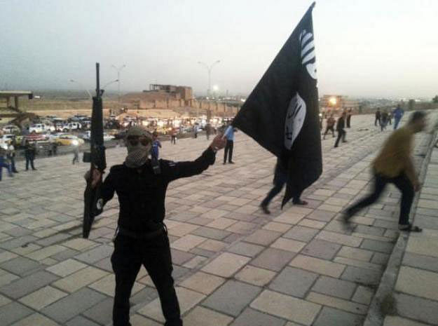 A fighter of the Islamic State of Iraq and the Levant (ISIL) holds an ISIL flag and a weapon on a street in the city of Mosul on 23 June 2014. File photo: Reuters