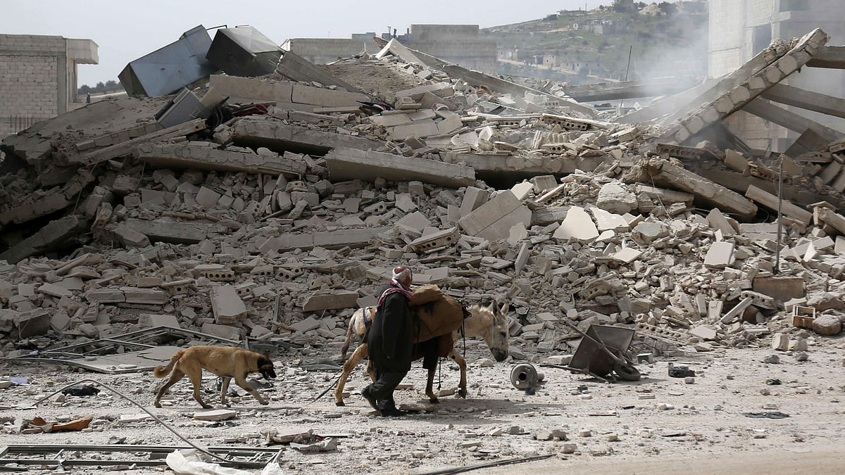 A picture taken on 22 March, 2018 shows a man walking with a loaded donkey and followed by a dog past the rubble of a destroyed building in the northwestern Syrian city of Afrin. Photo: AFP