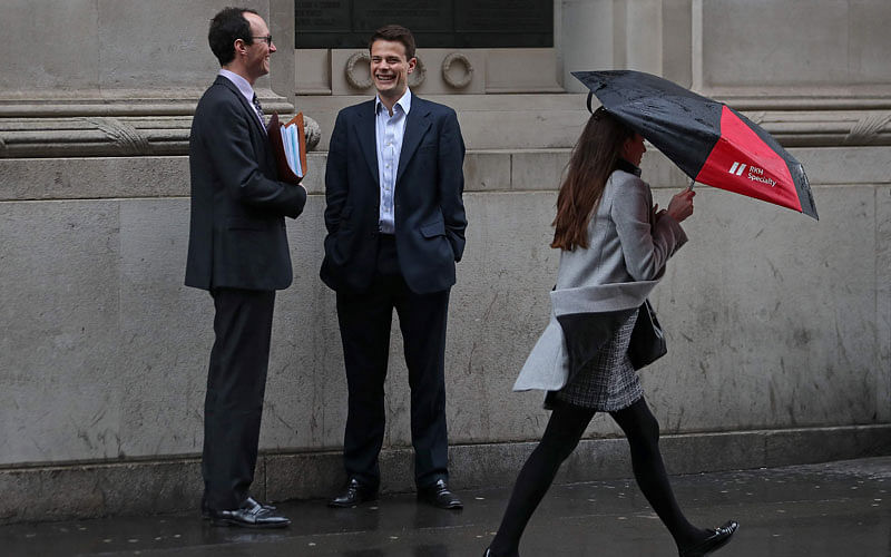A woman shelters from the rain beneath an umbrella as she walks past talking men in the City of London on Wednesday. AFP