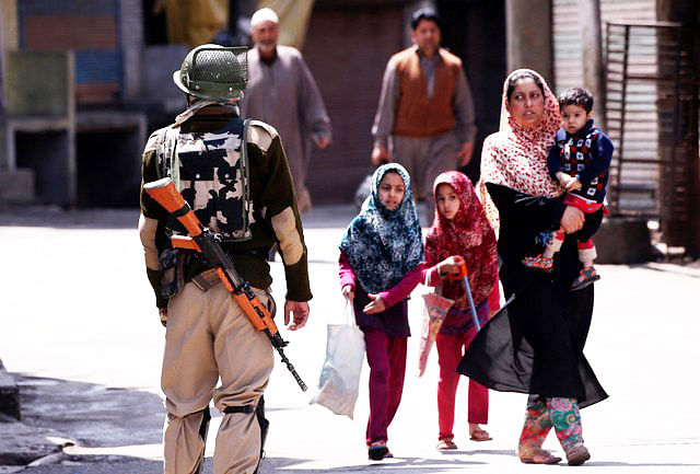 An Indian police officer stands guard, as people walk past him, during a strike called by Kashmiri separatists against the recent killings in Kashmir, in downtown Srinagar April 12, 2018. Photo : Reuters