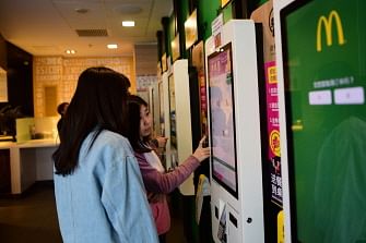 This picture taken on April 11, 2018 shows customers inputting orders with a self-service machine at a McDonald`s restaurant in Beijing. Photo : AFP