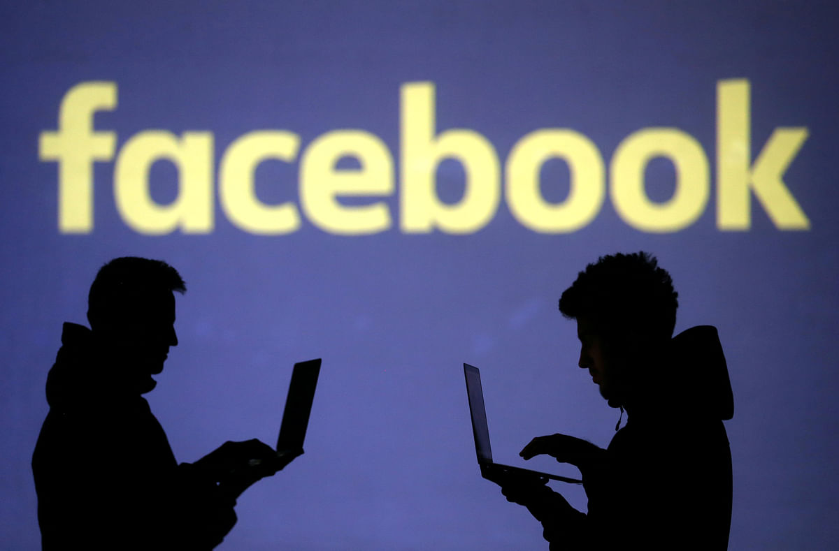 Silhouettes of laptop users are seen next to a screen projection of Facebook logo in this picture illustration. Photo: Reuters
