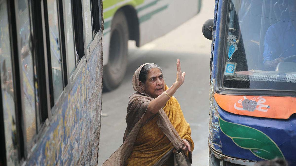 A woman makes her way through a narrow space between two buses near Shyamoli intersection in Dhaka on 17 April. Photo: Zahidul Karim