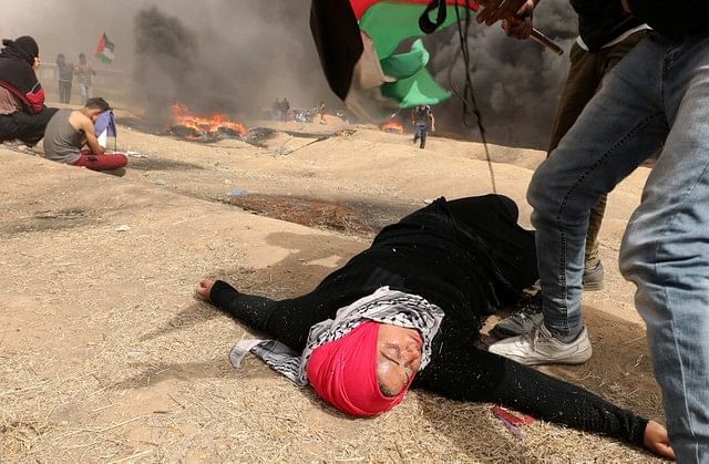 A woman demonstrator lies on the ground after inhaling tear gas fired by Israeli troops during clashes at a protest where Palestinians demand the right to return to their homeland, at the Israel-Gaza border, east of Gaza City April 20, 2018. Photo : Reuters