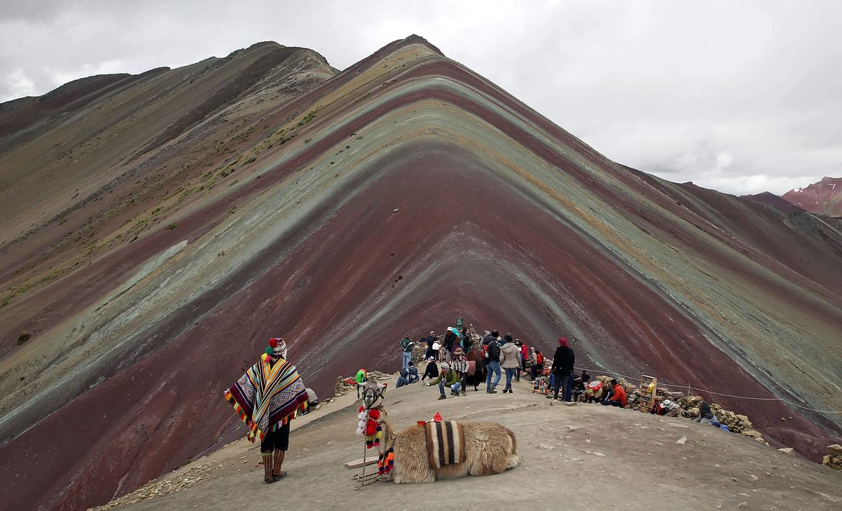 In this 2 March photo, an Andean man rests with his llama while tourists take in the natural wonder of Rainbow Mountain in Pitumarca, Peru. Photo: AP