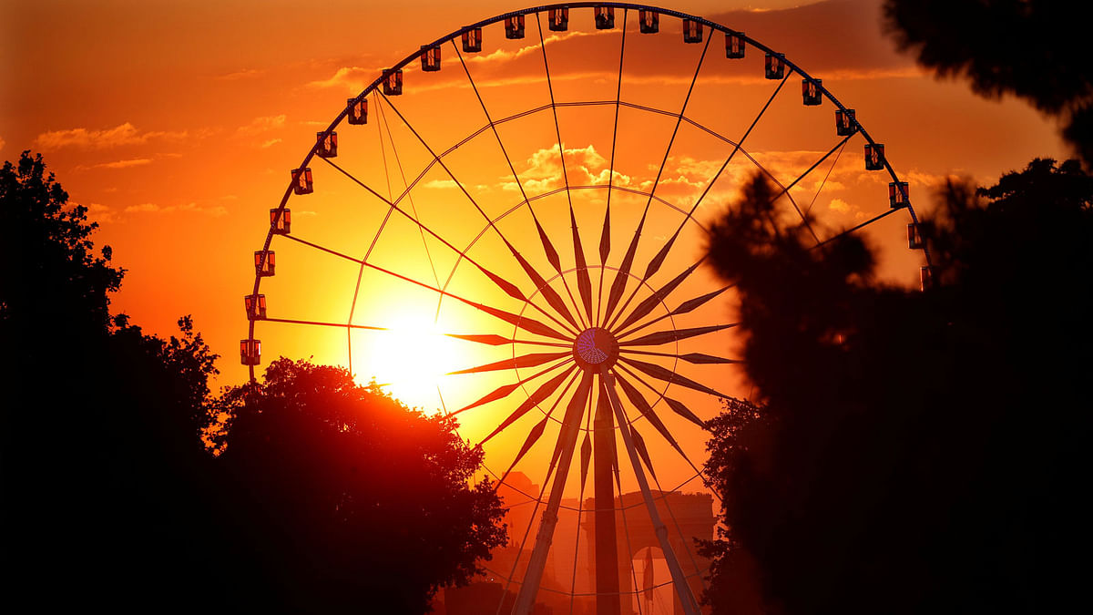 The sun is seen through the giant Ferris wheel on its way to the middle of the Arc de Triomphe at sunset during a phenomenon happening twice a year in Paris.