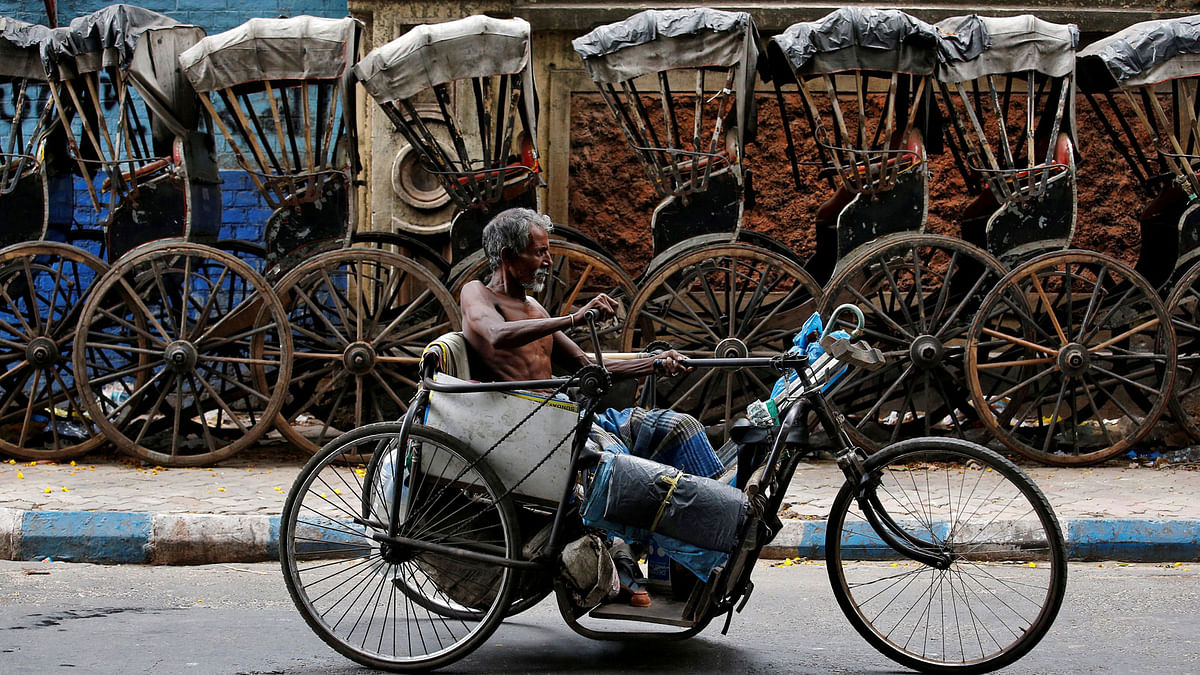 A disabled man paddles his tricycle as he moves past a row of parked hand-pulled rickshaws in Kolkata, India on 10 May.  Photo: Reuters