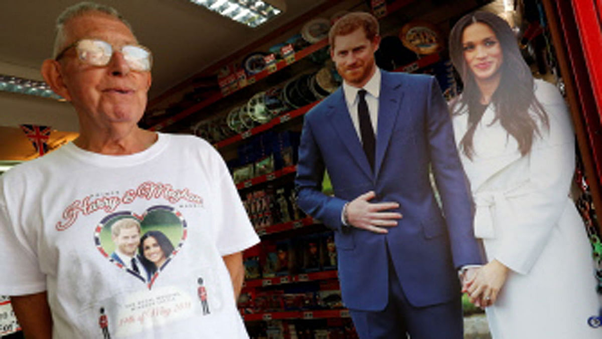 A man wears a Royal wedding souvenir t-shirt as he passes a life-size picture of Britain`s Prince Harry and his US fiancee Meghan Markle on leaving a gift shop near Windsor Castle in Windsor, west of London on May 15, 2018, as preparations get underway for the forthcoming Royal wedding. Photo : AFP