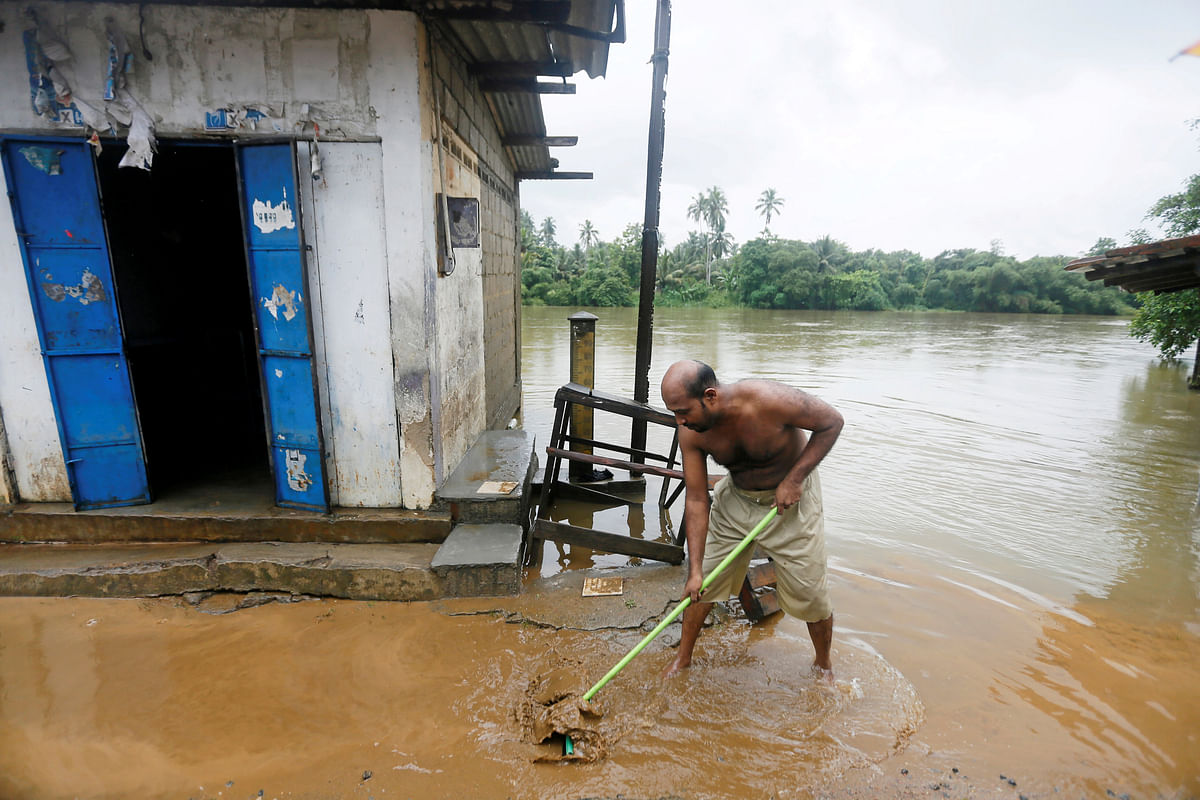 A man wipes mud in front of a shop after the river overflow due to heavy rains in Malwana, Sri Lanka on 23 May 2018. Photo: Reuters