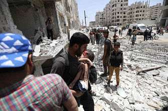 A man carries a wounded child out of a building following a car bomb explosion in the northern Syrian city of Idlib on May 26, 2018. Photo : AFP  Russia forces among dozens dead in IS east Syria attacks