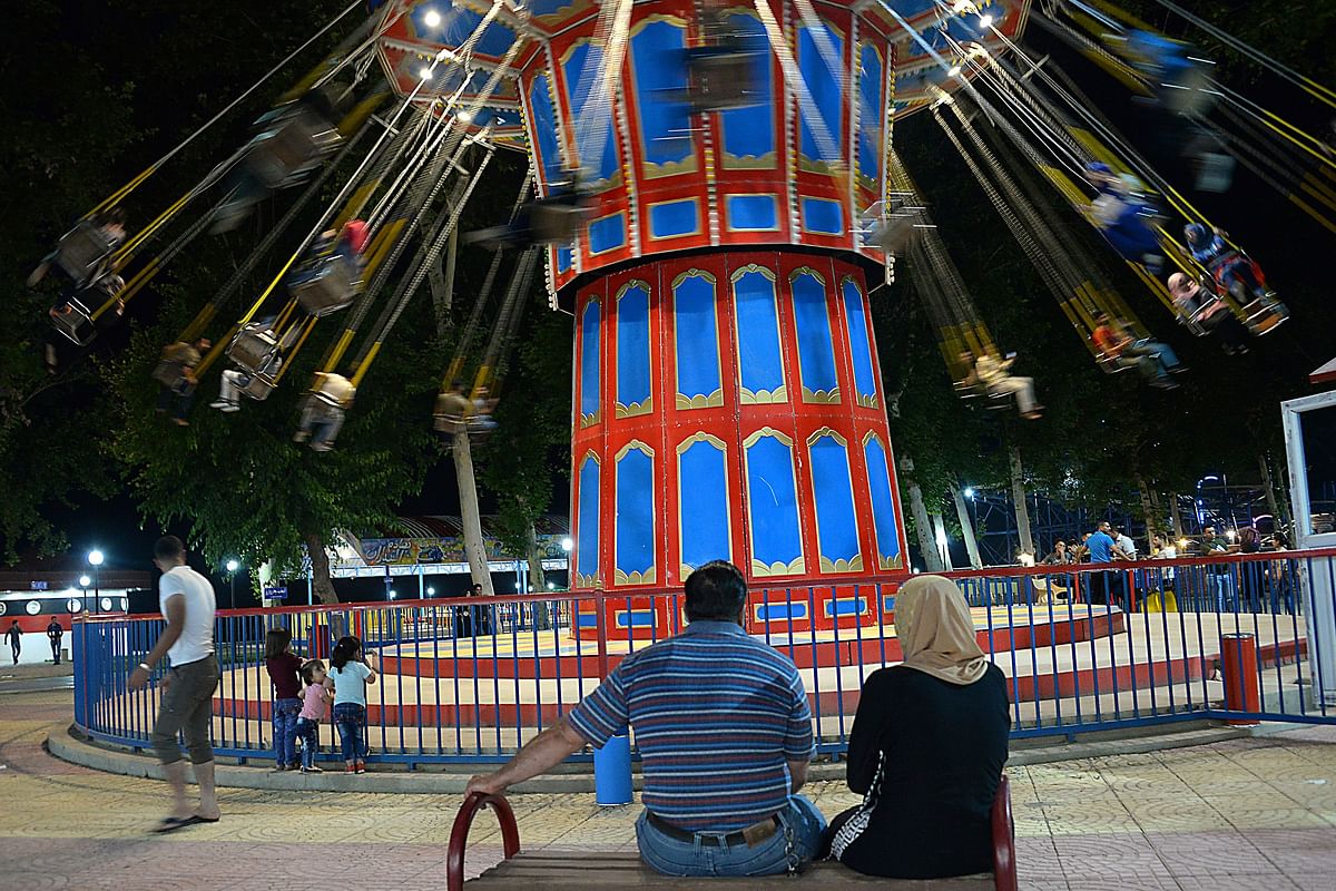 An Iraqi couple watches a merry-go-round after breaking the fast during the holy month of Ramadan in Mosul on 24 May 2018. The Islamist State (IS) group which controlled the city for three years before its ouster last July had banned the drumming, along with other traditions that make up the festive spirit of the month of dawn-to-dusk fasting. Photo: AFP