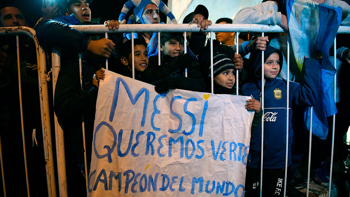 Children stand behid a fence holding a banner in support of Argentina`s forward Lionel Messi, outside the Argentine Football Association (AFA) training facilities in Ezeiza, Buenos Aires on May 30, 2018 as Argentina`s national football team heads to the airport, to travel to Barcelona for the last stage of preparation ahead of the FIFA World Cup 2018.  Photo:  AFP