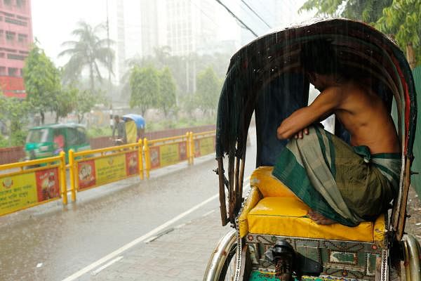 A rickshaw puller tries to save himself taking shelter under the hood of his rickshaw as he watches the rain. Dainik Bangla area, Dhaka, 1 June. Photo: Sumon Yusuf