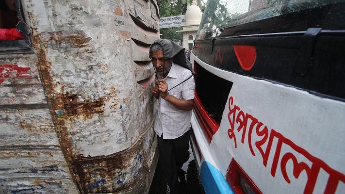 A pedestrian crosses the road through a narrow space between two buses in front of the Bar Council Bhaban at Mawlana Bhashani Road, Dhaka, 4 June. Photo: Abdus Salam