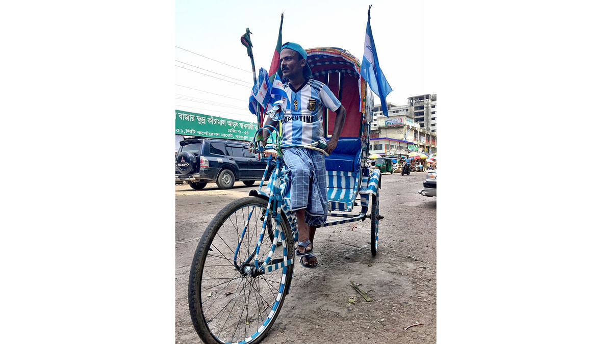As FIFA World Cup fever grips the country, football fans in Bangladesh have already adopted favourite countries as their own. The country is awash with flags of Argentina, Brazil, Germany and other countries. Football enthusiast Abu Taher `Messi`, is a rickshaw puller. He has painted his rickshaw in Argentina’s flag colours and hoisted several flags on 17 June in Karwan Bazar area of  Dhaka. Taher says, he does not let Brazil supporter as passengers in this rickshaw. Photo: Farjana Liakat
