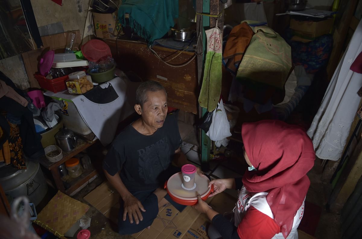 This picture taken on 20 March 2018 shows an elderly man (L) receiving a container with uneaten food from a volunteer of the programme `A Blessing to Share`, in a slum area in Jakarta. In the slums of Jakarta, Indonesia`s poor are getting a taste of how the other half live thanks to a new programme that aims to take a bite out of its mammoth food-waste problem. Photo: AFP