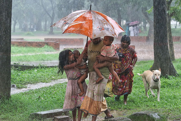 An entire family tries to fit under one umbrella in Suhrawardy Udyan in Dhaka on 25 June. Photo: Syful Islam