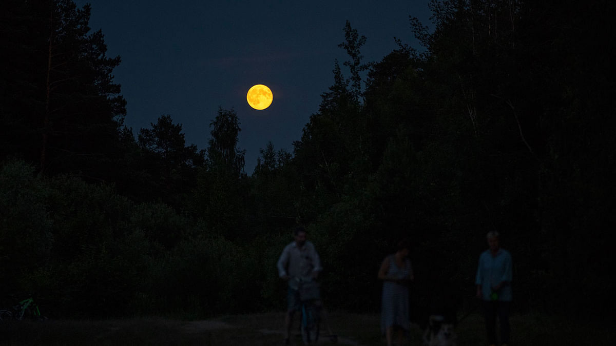 A full moon rises behind a forest as people stroll at the 2018 soccer World Cup in Kratovo, outskirts Moscow, Russia on 28 June 2018. Photo: AP