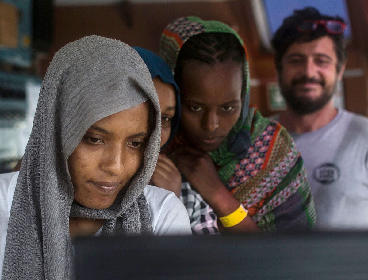 In this photo taken on 2 July migrant women look at a crew`s computer aboard the Open Arms aid boat, of Proactiva Open Arms Spanish NGO. Spain`s government said Barcelona will be the docking port for the aid boat travelling with 60 migrants rescued on Saturday in waters near Libya and rejected by both Italy and Malta. Photo: AP