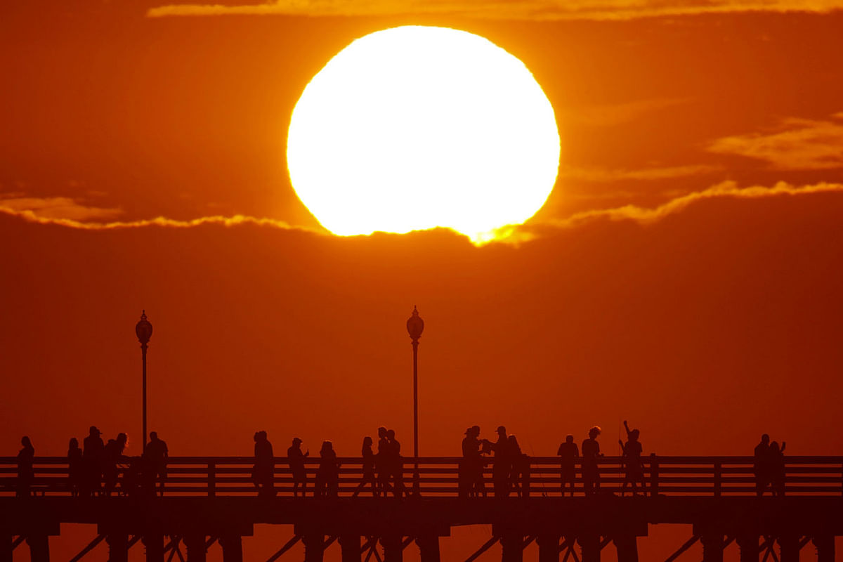 The sun sets behind a cloud as people cool off with a walk along an ocean pier in Oceanside, California, US, on 5 July 2018. Photo: Reuters