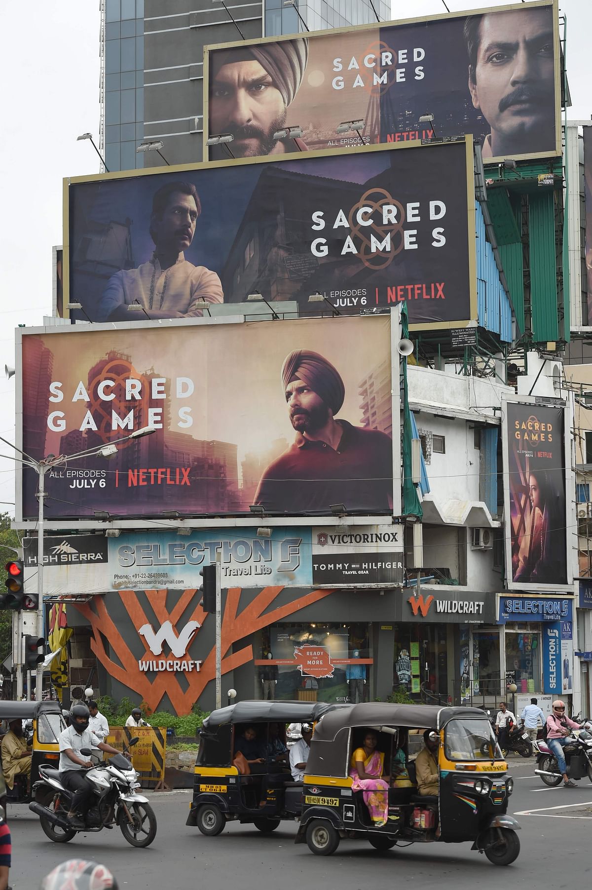 This photo taken on 4 July, 2018 shows Indian commuters travelling past large billboards for `Sacred Games`, the upcoming Indian series on Netflix, in Mumbai. Photo: AFP