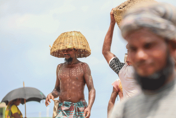 A worker covers his head with bamboo basket from scorching sunlight in Rupsha Kheyaghat area of Khunla on 11 July 2018. Photo: Saddam Hossain