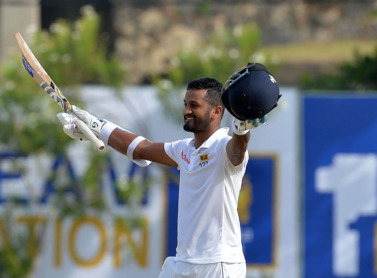 Sri Lankan cricketer Dimuth Karunaratne raises his bat and helmet in celebration after scoring a century (100 runs) during the first day of the opening Test match between Sri Lanka and South Africa at the Galle International Cricket Stadium in Galle on 12 July, 2018. Photo: AFP