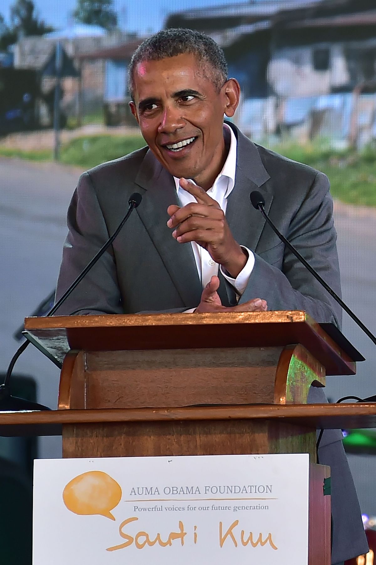Former US president, Barak Obama, gestures as he makes an address on 16 July, 2018 against a projected backdrop of a section of his father`s home village, the hamlet of Nyang`oma in Kogelo, during the opening of the Sauti Kuu Resource Centre, founded by his half-sister, Auma Obama at Kogelo in Siaya county, western Kenya. Photo: AFP