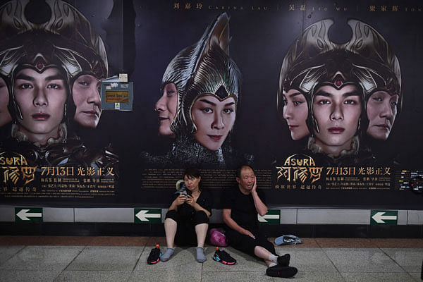 A man and woman rest in front of posters for the movie Asura at a subway station in Beijing on 17 July 2018. Pulled from cinemas after its opening weekend, China`s most expensive domestically made film has become a flop of historic proportions, bringing in just 7.3 million USD despite a reported budget of over 110 million USD. Photo: AFP