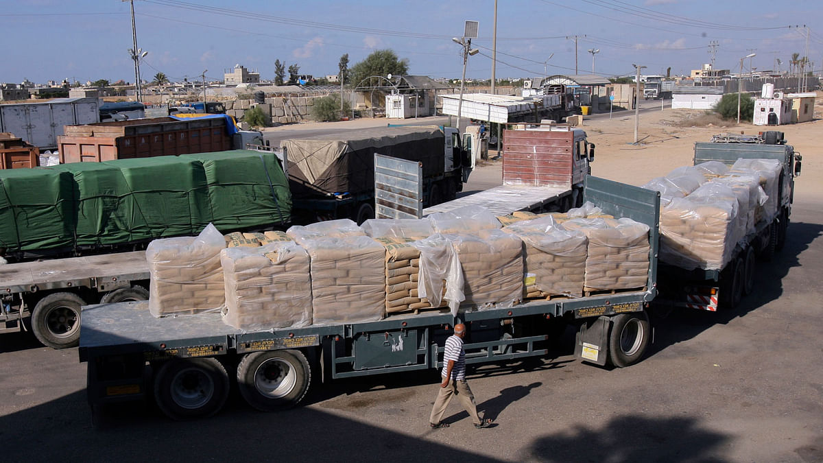 In this 14 October 2014, file photo, a Palestinian worker walks next to trucks loaded with sacks of cement at the Kerem Shalom border crossing on its way from Israel to Rafah in the southern Gaza Strip. Israel shut down the cargo crossing of Kerem Shalom with the Gaza Strip on Tuesday in response to continued Hamas hostilities, even after it agreed to a cease-fire ending 24 hours of intense fighting. Photo : AP