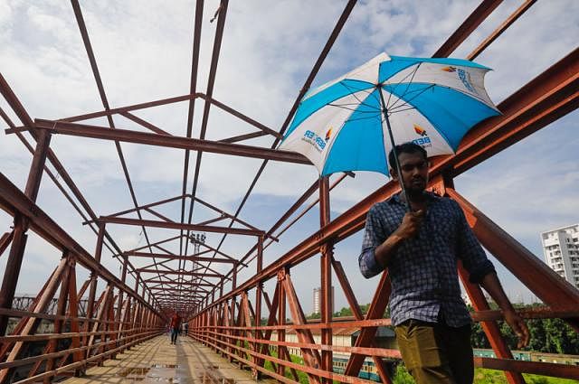 A man crosses the Sabujbag section of Kamalapur foot over-bridge with an umbrella on 17 July. There is no roof of the bridge to save pedestrians from scorching sun. Photo: Dipu Malakar