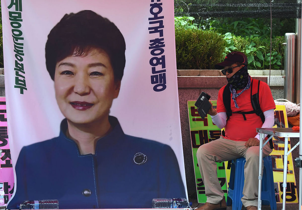 A supporter of South Korea`s former president Park Geun-hye looks at his smartphone next to a picture of Park during a protest demanding her release outside the Seoul Central District Court in Seoul on 20 July. Photo: AFP