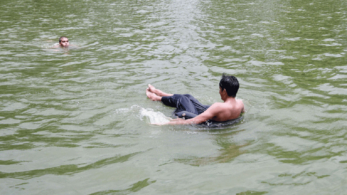 A man swims in the pond while another person floats with a tyre in scorching heat of 20 July. The picture has been taken from Polytechnic Institute, Pabna on 20 July. Photo: Abdus Salam.