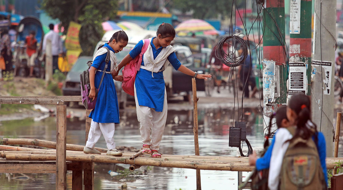 Students on a bridge near the Agrabad Talebia Government Primary School in Chattogram. The teachers and students of the school suffer everyday as they have to cross muddy water on their way to school. Road repairs cause the sufferings. A recent photo by Jewel Shil