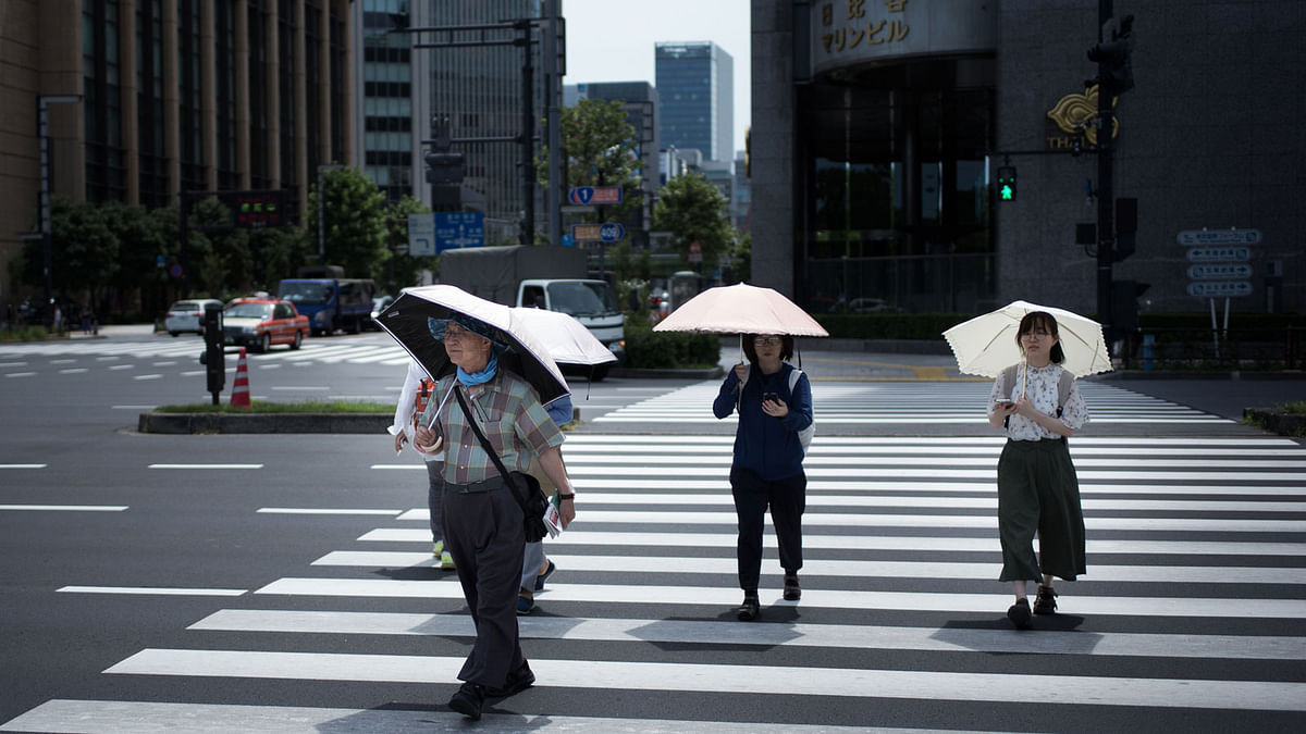 People hold umbrellas as they walk along a street in Tokyo on 23 July 2018, as Japan suffers from a heatwave. Photo: AFP