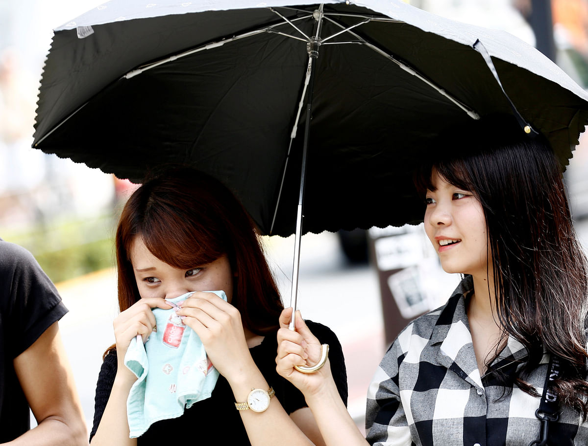 A woman wipes her face and another woman holds a parasol on the street during a heatwave in Tokyo. Reuters
