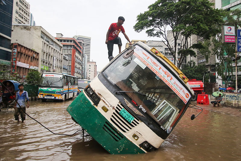 People try to pull a bus as it tilted dangerously after falling into a waterlogged ditch in Motijheel area of Dhaka on 23 July. Photo: Saiful Islam