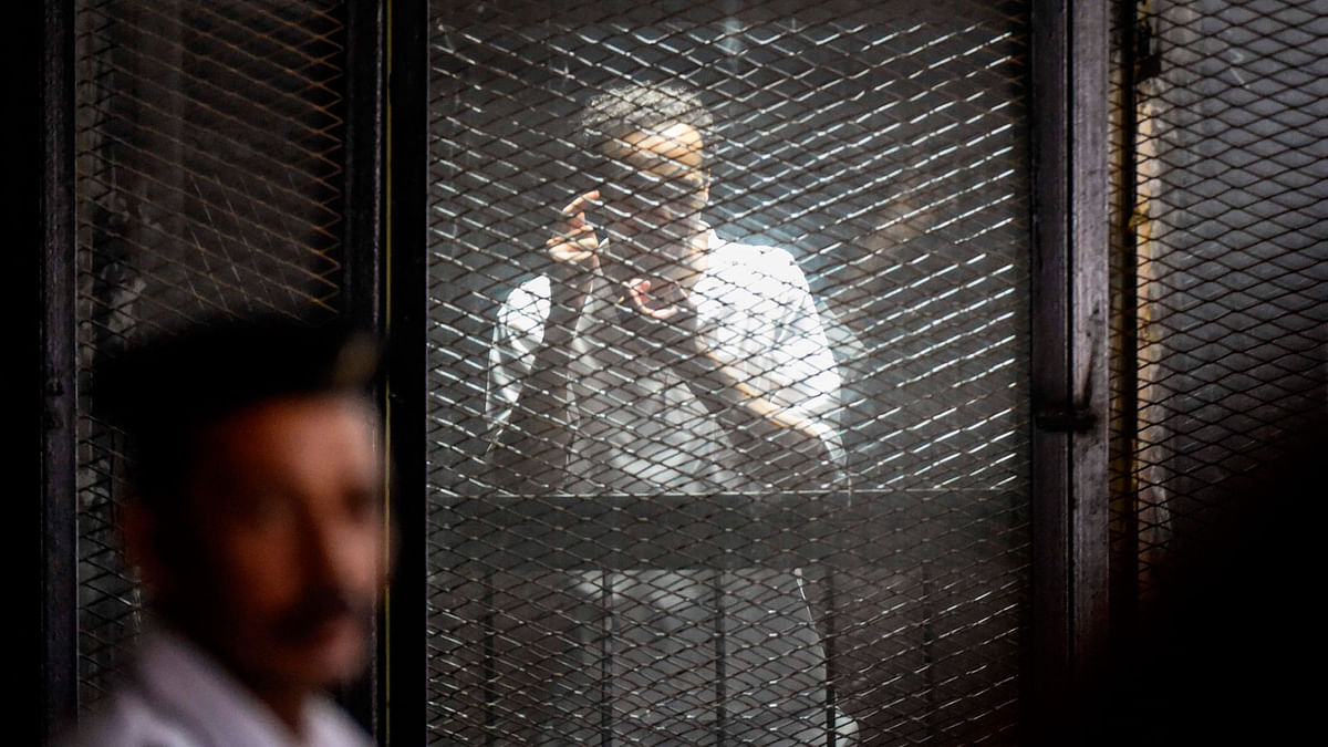 Egyptian photographer Mahmoud Abdel Shakour Abouzied, also known as Shawkan, makes a gesture mimicking taking a photograph from inside a soundproof glass dock, during his trial in the capital Cairo on 28 July 2018. -- AFP