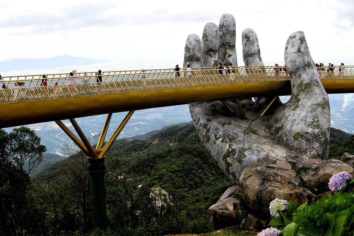 In this photograph taken on 31 July 2018, visitors walk along the 150-meter long Cau Vang `Golden Bridge` in the Ba Na Hills near Danang. Nestled in the forested hills of central Vietnam two giant concrete hands emerge from the trees, holding up a glimmering golden bridge crowded with gleeful visitors taking selfies at the country`s latest eccentric tourist draw. -- AFP