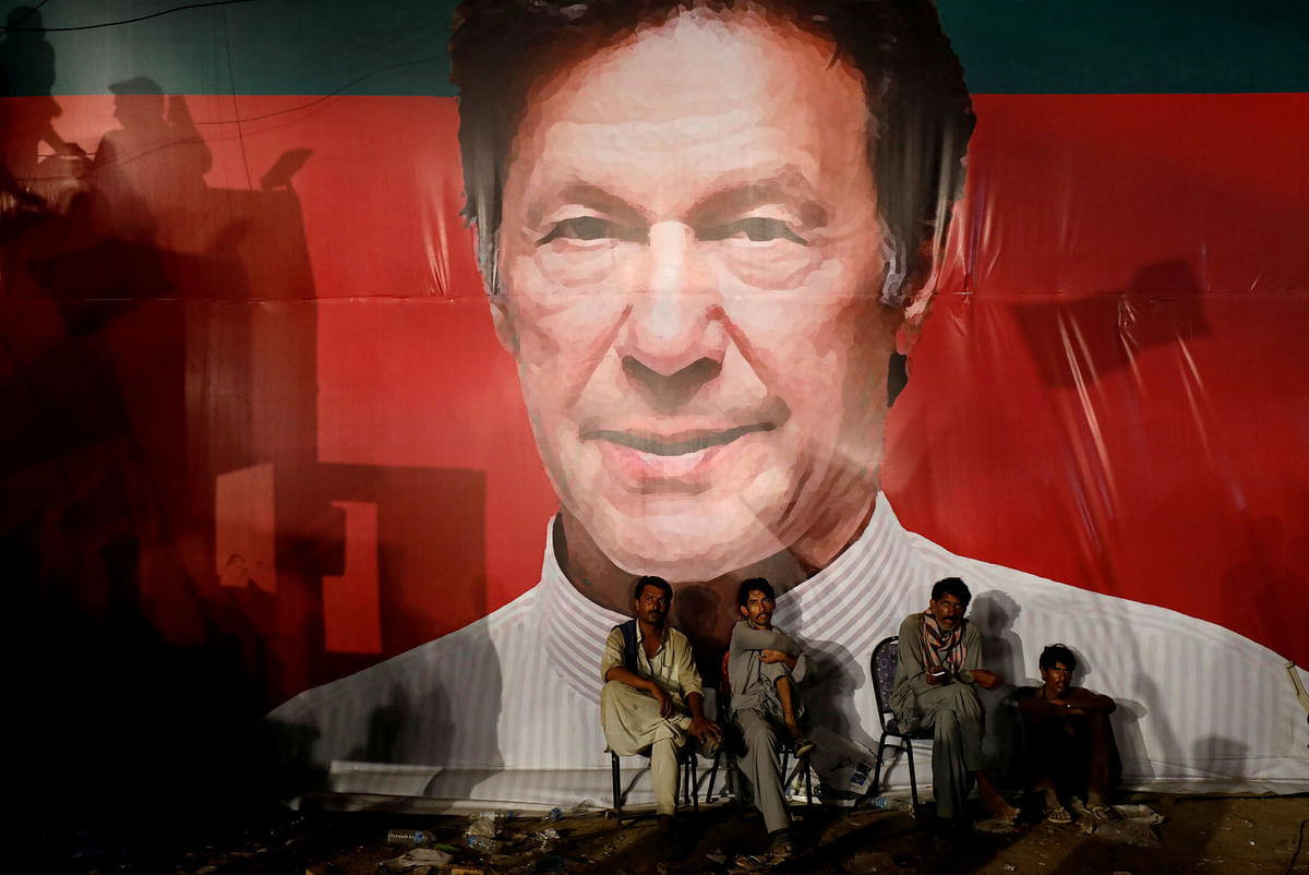 Labourers, who set up the venue, sit under a wall with a billboard displaying a photo of Imran Khan, chairman of the Pakistan Tehreek-e-Insaf (PTI), political party, as they listen to him during a campaign rally ahead of general elections in Karachi, Pakistan on 22 July 2018. Reuters File Photo