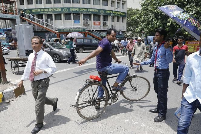 A boy scout holding an umbrella regulates traffic at Shahbagh, Dhaka on Monday. Scout members from different schools have been deployed with the traffic police on roads to observe the traffic week. Photo: Dipu Malakar