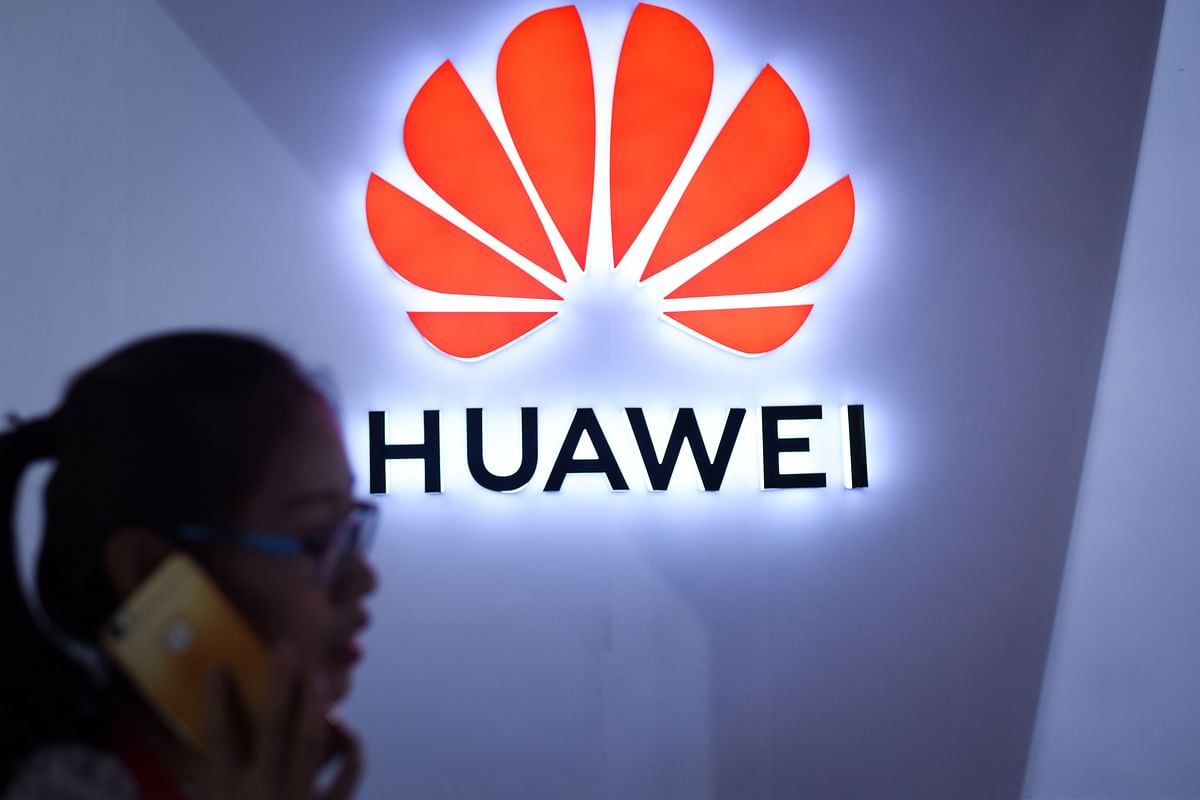 This file picture taken on 9 July 2018 shows a woman using her mobile phone in front of a LED display board of Huawei at Beijing International Consumer Electronics Expo in Beijing. Photo: AFP