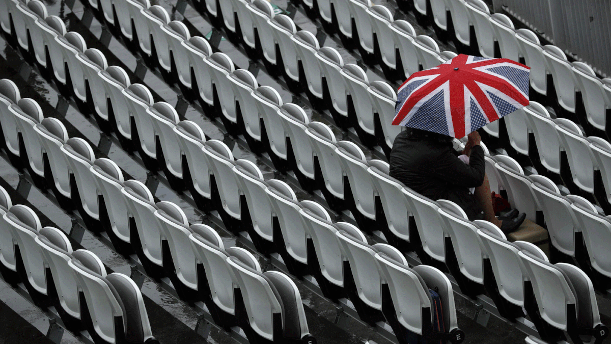 A cricket fans sits beneath an umbrella as rain delays play on the first day of the second Test cricket match between England and India at Lord`s Cricket Ground in London on 9 August 2018. - AFP