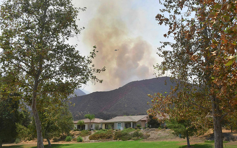 A helicopter flies over a plume of smoke from fires still burning at a Cleveland National Forest hillside near the senior retirement community of Trilogy at Glen Ivy in Corona, California on 13 August, 2018. Photo: AFP