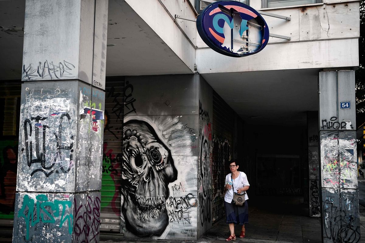 A woman walks past a Greek Manpower Employment Organisation building covered in graffiti and which sign is smashed in central Athens, on 9 August 2018. On 20 August, Greece`s third and final bailout officially ends after years of hugely unpopular and stinging austerity measures. The economy is growing slowly, and unemployment fell to below 20 per cent in May for the first time since 2011. -- AFP