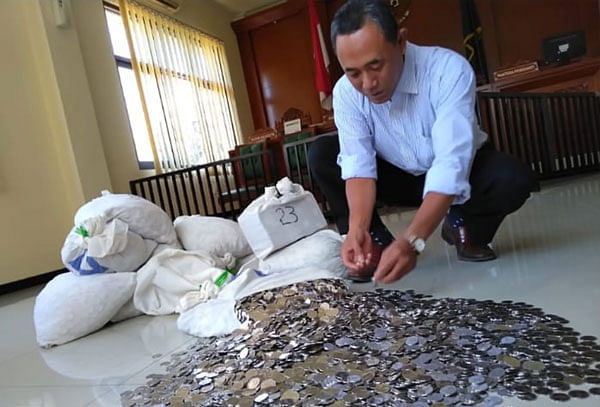 In this handout picture taken on August 23, 2018 and released by Dhe Sutarto on August 24, 2018 shows Dwi Susilarto hauling a dozen sacks filled with 153 million rupiah ($10,500) in small change, after arriving at the court in Solo, Central Java, as a hefty payment that weighed in at about 890 kilograms (1,960 pounds).  Photo: AFP