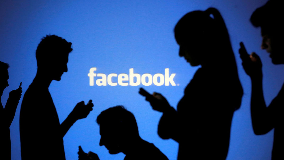 People are silhouetted as they pose with mobile devices in front of a screen projected with a Facebook logo, in this picture illustration on 29 October 2014. Reuters File photo