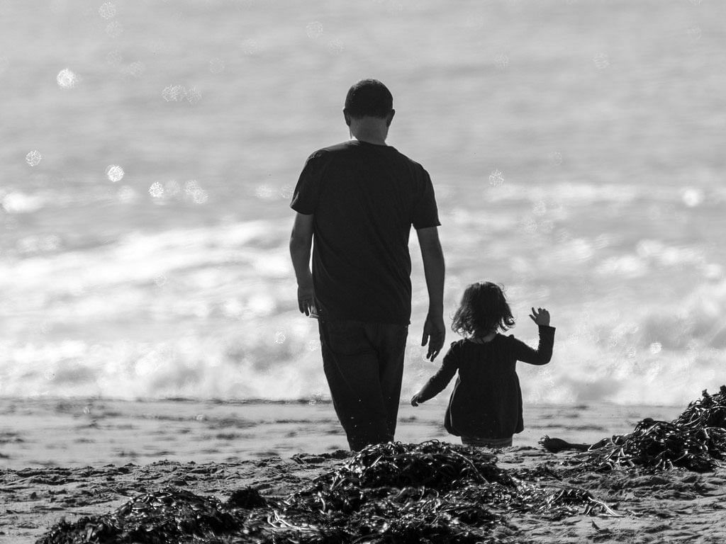 Father and daughter walking on a beach. Photo: Collected